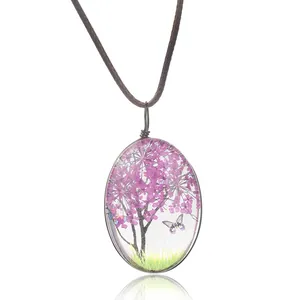 Gros plan du pendentif ovale en résine avec fleurs séchées violettes et papillon