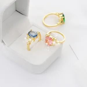 Ensemble de trois bagues dorées avec cristaux ovales bleus, roses et verts dans un écrin