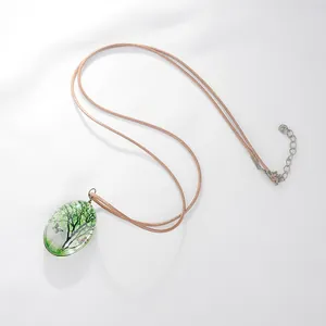 Détail du collier pendentif ovale avec motif d'arbre et papillon sur fond blanc texturé