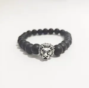 Primer plano de pulsera con cuentas negras mates y dije de cabeza de león plateado sólido