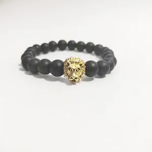 Primer plano de pulsera con cuentas negras mates y detalle de cabeza de león dorada