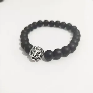 Pulsera de cuentas negras mate con dije de cabeza de león plateada sobre fondo blanco