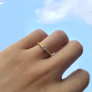 Close-up of a delicate gold ring with a round zircon stone against a blue sky