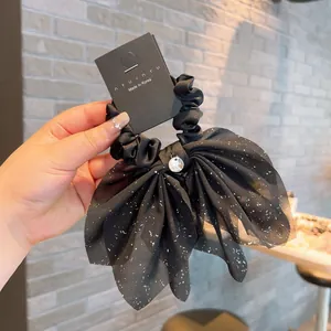 Detail of black bow hair scrunchie with shimmering silver star glitter and metallic pendant