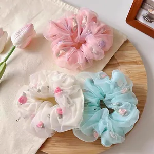 Three mesh flower scrunchies in pink, white and blue colors with delicate rose ornaments
