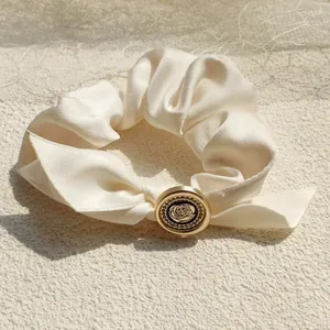 Detail of elegant cream silk scrunchie with rose button and sparkling rhinestone accents