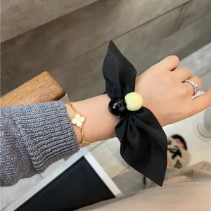 Black satin bow scrunchie with decorative beads worn on wrist in a lifestyle setting