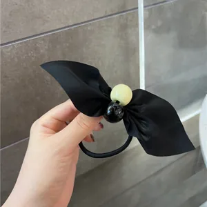 Elegant black silk bow hair tie with decorative beads shown on hand over marble background