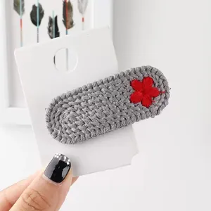 Detailansicht der handgefertigten grauen Strickhaarklammer mit einer roten Stickblume