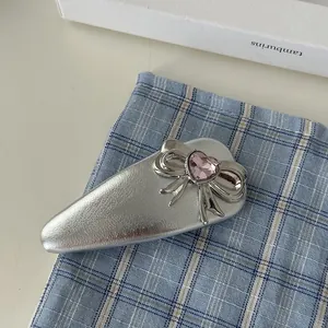Detail of silver bow hair clip with pink heart gemstone on a blue checkered background