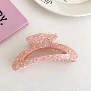 Detail of pink marble textured acetate hair claw clip on a stylish white surface