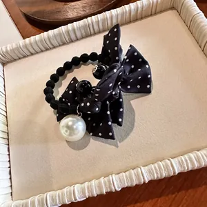 Détail d'un chouchou à nœud à pois noirs avec une grande perle et des perles sur un plateau