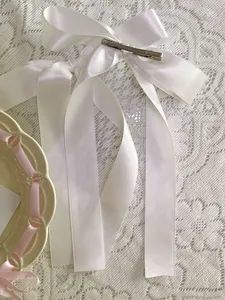 Detailed view of white satin bow hair clip with silver crocodile clip on lace background