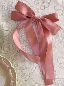 Close-up of pink satin multi-layer bow hair clip with long ribbons on lace background