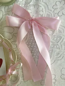 Detail of light pink satin ribbon hair bow with long streaming ties on lace background