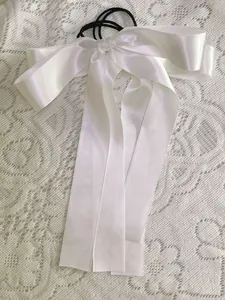 Detail of white satin bow hair tie with long ribbons on an elegant lace background
