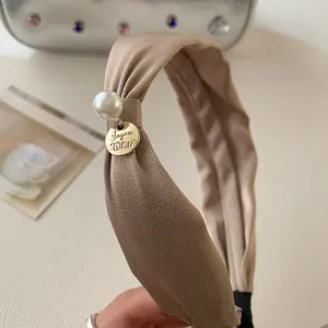 Detail of khaki fabric headband with white pearl and golden Jayna White brand tag