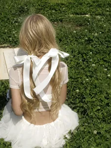 Detail of a creamy white satin ribbon bow hair clip with long streamers in sunlight