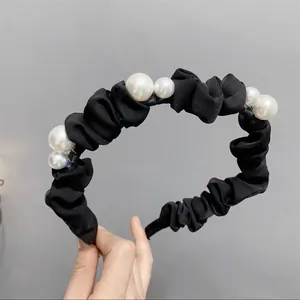 Détail d'un serre-tête en tissu noir froncé orné d'élégantes perles blanches nacrées