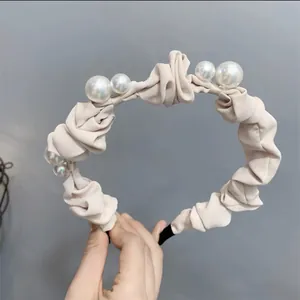Détail du serre-tête en satin froissé beige orné de perles blanches élégantes