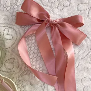 Pink satin ballet ribbon bow hair tie with long streamers on white lace background