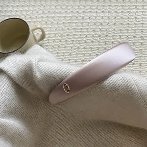 Detailed close-up of a pale pink satin headband with a golden oval metal emblem detail