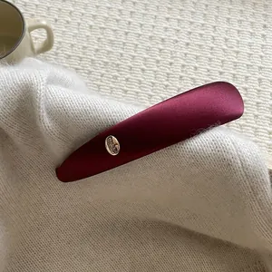 Close-up of wine red satin hair clip with oval metal tag on white knit sweater