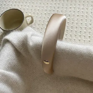 Elegant champagne satin padded headband featuring a gold-tone BELIEVE metal plaque charm
