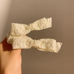 Close-up of cream white embossed fabric hair clips with wavy edges and soft 3D texture