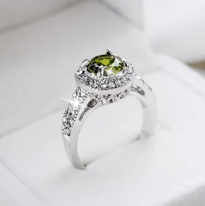 Vista macro de un anillo de cristal verde oliva con halo de diamantes en joyero blanco