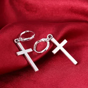 Macro detail of silver cross earrings on elegant red silk fabric background