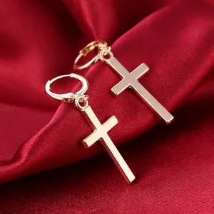 Macro shot of polished gold cross drop earrings on a smooth red silk fabric background