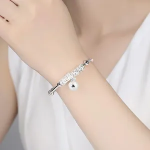 Detailed view of a silver-colored bangle featuring hollow beads and a bell charm pendant