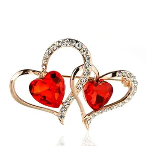 Detalle de un broche de doble corazón de cristal rojo en oro rosa con pedrería brillante