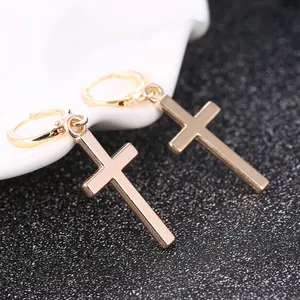 Polished gold cross dangle earrings with secure hoop closure on a white ceramic tray