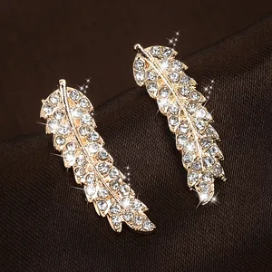 Detailed macro view of golden feather earrings with sparkling crystal pavé on silk