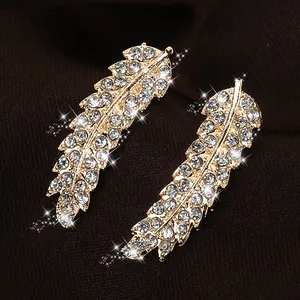Macro shot of gold feather stud earrings with sparkling rhinestones on silk background