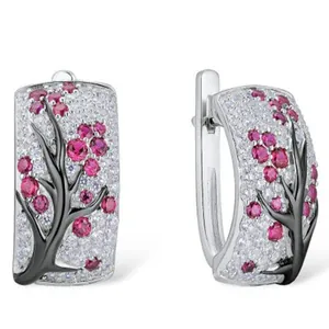 Detailed close-up of silver flower huggie earrings with pink crystals and black branches