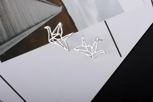 Detalle de los pendientes de grulla origami plateados con diseño de líneas caladas finas