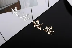 Detalle macro de pendientes de grulla origami dorados y plateados geométricos