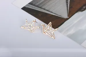 Detalle de pendientes de grulla dorados con diseño geométrico sobre fondo blanco liso
