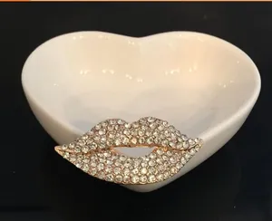 Funkelnde Strass-Lippenbrosche mit goldfarbener Legierung auf einer Herz-Keramikschale