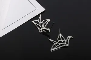 Primer plano de pendientes de origami de plata pulida sobre una superficie de espejo negra