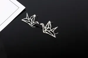 Primer plano de aretes de grulla en origami sobre una superficie de espejo negra