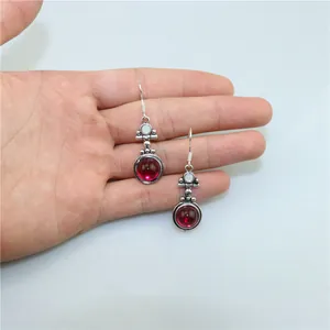 Detail of vintage silver earrings with red teardrop stone held for size reference