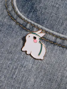 Cute white bunny enamel pin with green ribbon detail pinned on blue denim jacket