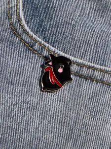 Detail of a cartoon pig enamel pin with a red scarf on denim fabric background