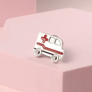 Modern silver ambulance enamel brooch with red cross accent on a pink background