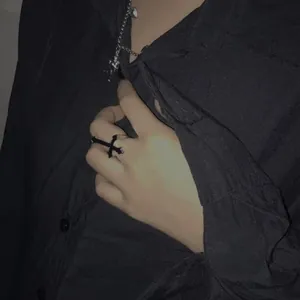 Close-up of black metal cross ring and silver chain necklace worn with a dark shirt
