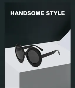 Macro detail of oval sunglasses featuring thick black resin frames and dark tinted lenses
